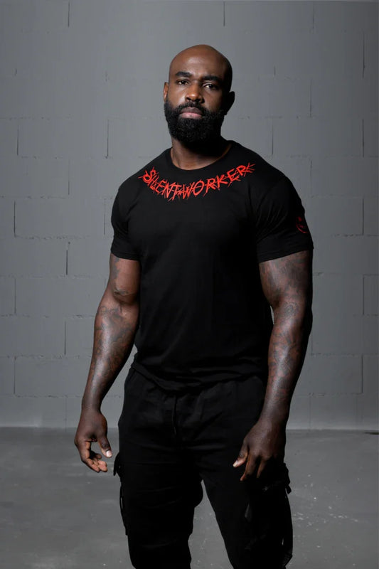 Man wearing Silent Worker black powerlifting t-shirt, standing in studio with gray wall