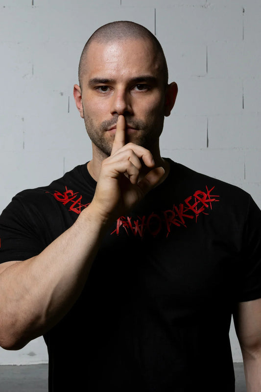 Man in Silent Worker powerlifting t-shirt making shushing gesture, minimalist background